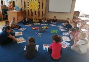Dzieci siedzą na dywanie w kole układają obrazek z figur geometrycznych